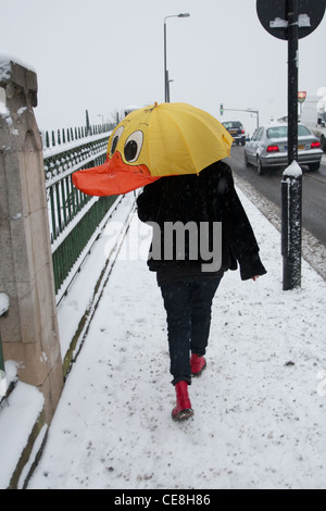 Eine Frau überquert eine Brücke im Schnee mit einem hellen farbigen Ente Schirm schützt ihr aus dem Schnee Stockfoto