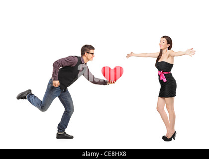 Freund mit einem roten herzförmige Kissen in der Hand und einem aufgeregt Freundin erweitern ihre Arme laufen Stockfoto