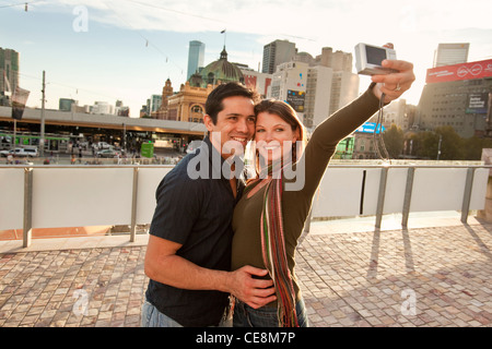 Paar, wobei ein Selbstporträt mit Skyline der Stadt im Hintergrund bei Sonnenuntergang. Federation Square, Melbourne, Victoria, Australien Stockfoto