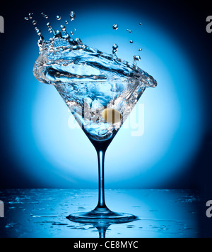 Splash Martini vor herumfliegenden Oliven. Objekt auf blauem Grund. Stockfoto