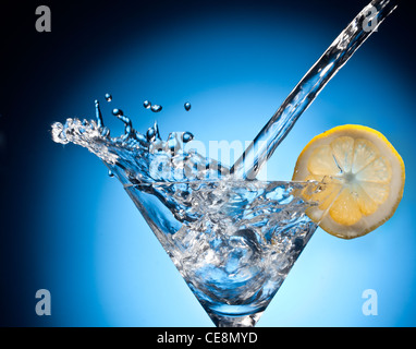 Spritzen von strömenden Martini in das Glas. Objekt auf blauem Grund. Stockfoto