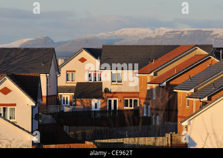 Häuser in einem schottischen moderne Anwesen durch die Wintersonne Abend und Campsie Hills auf der Rückseite beleuchtet mit Schnee bedeckt. Stockfoto