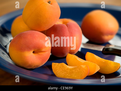 Ganze und geschnittene Aprikosen auf einer blauen Keramikplatte. Stockfoto