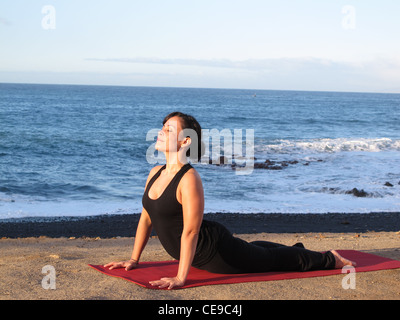 Schöne Frau dabei Hatha Yoga am Strand, nach oben mit Blick auf Hund Stockfoto