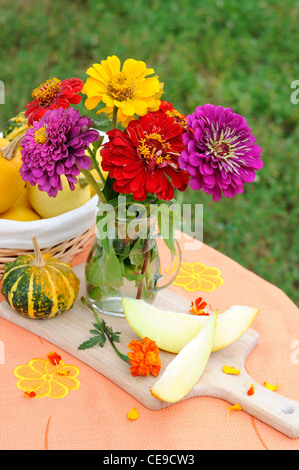 Stillleben mit Herbstblumen, Scheiben Melone und Kürbis. Stockfoto