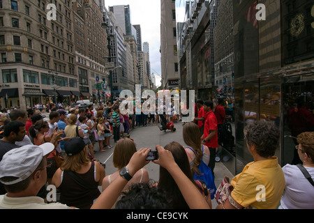 Dutzende von Menschen sehen vier afroamerikanische Männer in roten Hemden eine Breakdance-Routine auf dem Bürgersteig der 5th Avenue in New York durchführen Stockfoto