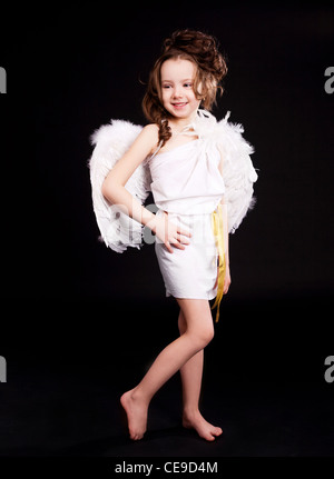 niedliche sechs Jahre alten Mädchen, gekleidet wie ein Amor mit weißen Flügeln, Pfeil und Bogen, isoliert gegen schwarze Studio-Hintergrund Stockfoto