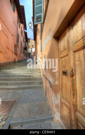 Vertikal ausgerichtete Bild der Holztür und schmale gepflasterte Straße zwischen alten Häusern in der Stadt von Saluzzo, Norditalien. Stockfoto