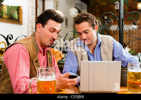Zwei Freunde in bayerischen Kneipe in traditioneller Kleidung auf einem Tisch in einer Kneipe mit laptop Stockfoto