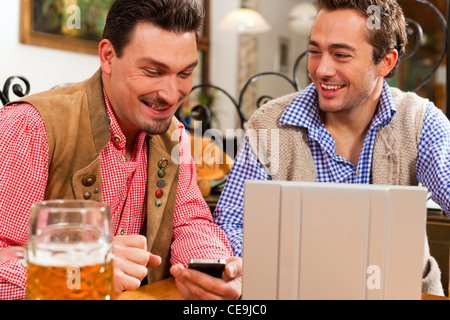 Zwei Freunde in bayerischen Kneipe in traditioneller Kleidung auf einem Tisch in einer Kneipe mit laptop Stockfoto