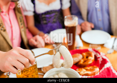 Gruppe von jungen Männern und Frauen in traditionellen bayerischen Tracht mit einem Frühstück mit weißen Weißwurst, Brezel und Bier Stockfoto