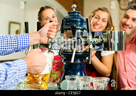 Mann ein Bier vom Hahn auf einem Kegerator im Pub oder Inn, Menschen in bayerischer Tracht Zeichnung stehen im Hintergrund Stockfoto