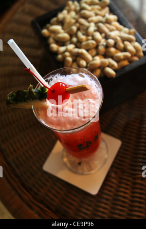 Ein Singapore Sling sitzt auf einem geflochtenen Tisch in der Long Bar in Singapur Raffles Hotel, wo der berühmte Cocktail entstanden. Stockfoto