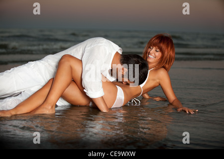glückliches, junges Paar, in weiß gekleidet, küssen, bei Sonnenuntergang an einem einsamen Strand Ufer umarmt Stockfoto