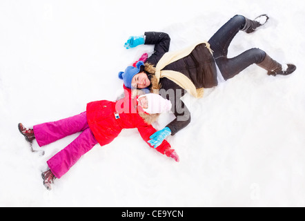 glückliche Familie; Mutter und Tochter machen Schnee-Engel an einem Wintertag im freien Stockfoto