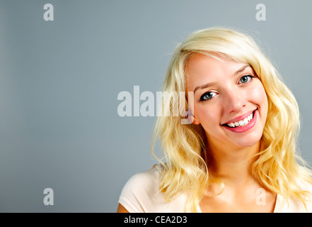 Porträt von lächelnden jungen blonden kaukasischen Frau auf grauem Hintergrund Stockfoto