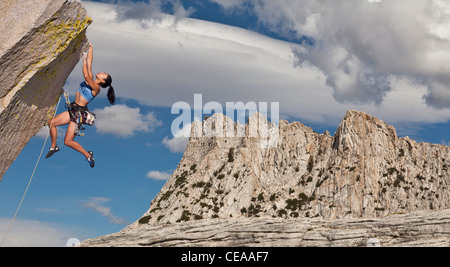 Weibliche Kletterer kämpft, um ihren nächsten Griff am Rande einer anspruchsvollen Klippe zu erreichen. Stockfoto