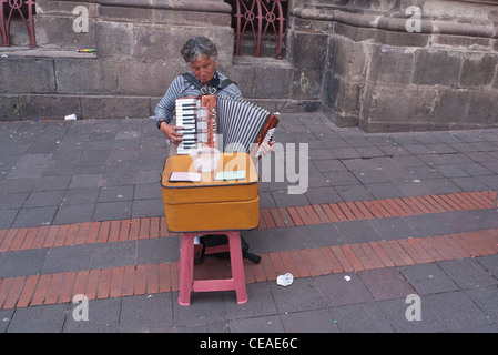 Ein blinder Straßenmusiker spielt Ziehharmonika, beim bitten um Geld, hinter seinem provisorischen Tisch in den Straßen, Quito, Ecuador. Stockfoto