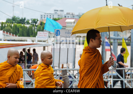 Senior Thai Mönch mit gelben Regenschirm, gefolgt von zwei Novizen verlassen der Fähre in Bangkok Thailand Stockfoto