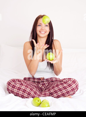 hübsches Mädchen auf dem Bett zu Hause sitzt und die Äpfel jonglieren Stockfoto