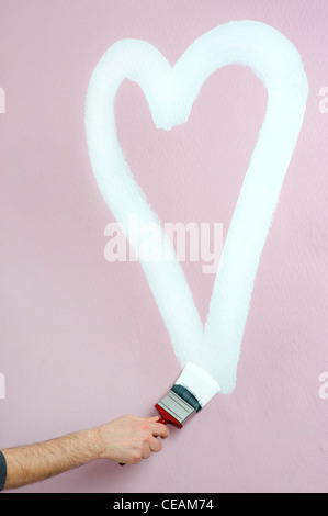 Person malt ein Herz auf einer rosa Wand Stockfoto