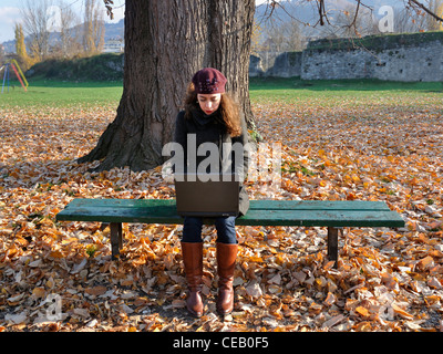 Junge Frau sitzt im Freien auf der Parkbank mit laptop Stockfoto