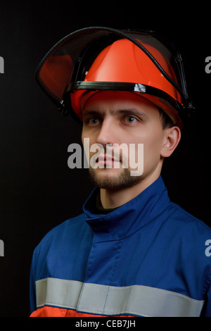 Die Arbeitskraft in Overall und Helm auf einem schwarzen Hintergrund Stockfoto