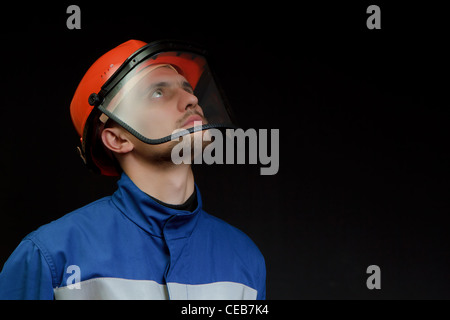 Die Arbeitskraft in Overall und Helm auf einem schwarzen Hintergrund Stockfoto