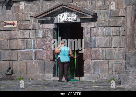 Ein Hispanic Frau Ladenbesitzer an die Kirche von San Francisco in Quito fegt den Bürgersteig außerhalb der Kirche Souvenirladen. Stockfoto