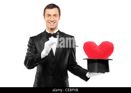 Junge Zauberer hält einen Zauberstab und Zylinder mit einem roten Herz geformten Kissen drin isoliert auf weißem Hintergrund Stockfoto
