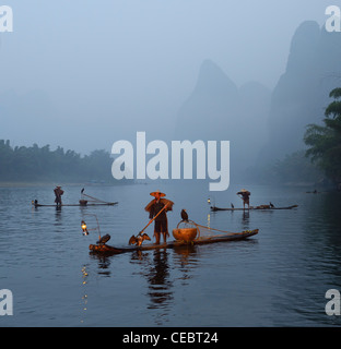 Kormoran Fischer auf dem Li-Fluss in der Morgendämmerung mit Karst Berggipfel im Nebel Xingpingzhen Yangshuo, Guilin, Guangxi, China Stockfoto