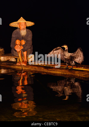 Kormoran Fischer und mit Ausbreitung Flügeln spiegelt sich in dem Li-Fluss in der Nacht von einem Bambusfloß Xingpingzhen Yangshuo, Guilin, Guangxi, China Stockfoto