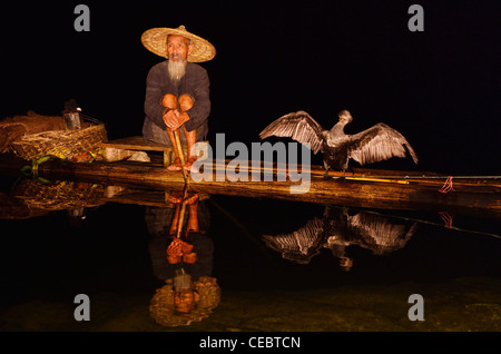 Kormoran Fischer und mit Ausbreitung Flügeln spiegelt sich in einer ruhigen Li-Fluss in der Nacht von einem Bambusfloß Xingpingzhen Yangshuo, Guilin, Guangxi China Stockfoto