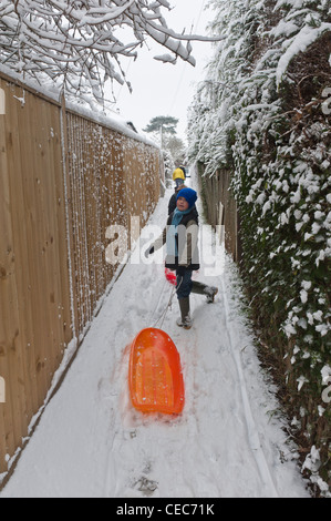 Tween-junge mit Schlitten in den Schnee zu Fuß Pisten mit seiner Familie und seinen Freunden. Hastings, East Sussex. England-UK Stockfoto