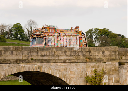 Bunt dekorierte indische Stil Bus über alte Brücke fahren in Yorkshire Dales (auf Lage, Dreharbeiten Sharwood's Anzeige Kampagne) - Burnsall, England, UK. Stockfoto