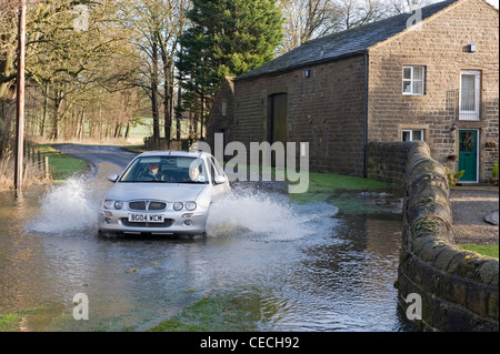 Überschwemmung - silver Auto (Rover) Fahren & Spritzwasser durch tiefe Hochwasser auf überfluteten Landstraße nach schweren Regenfällen - North Yorkshire, England, UK. Stockfoto