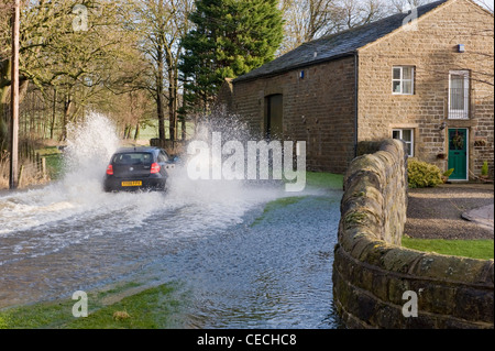 Überschwemmung - Schwarze Auto (BMW) Fahren & Spritzwasser durch tiefe Hochwasser auf überfluteten Landstraße nach schweren Regenfällen - North Yorkshire, England, UK. Stockfoto