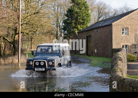 Überschwemmung - Land Rover Defender Fahren & Spritzwasser durch tiefe Hochwasser auf überfluteten Landstraße nach schweren Regenfällen - North Yorkshire, England, Großbritannien Stockfoto