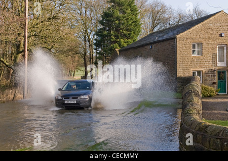 Überschwemmung - woman-driving-schwarzes Auto & Spritzwasser durch tiefe Hochwasser auf überfluteten Landstraße nach schweren Regenfällen - North Yorkshire, England, UK. Stockfoto