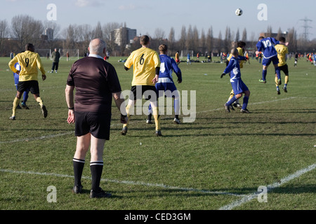 Schiedsrichter Uhren eine Ecke von Verteidiger gelöscht wird, zwei blaue und gelbe Mannschaften Sonntag Liga Sümpfe Hackney, London. Stockfoto