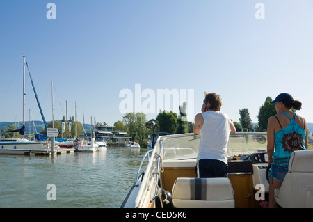 Horizontale Anzeigen eines Mannes und einer Frau an Bord ein Schnellboot fahren durch eine Marina an einem sonnigen Tag. Stockfoto