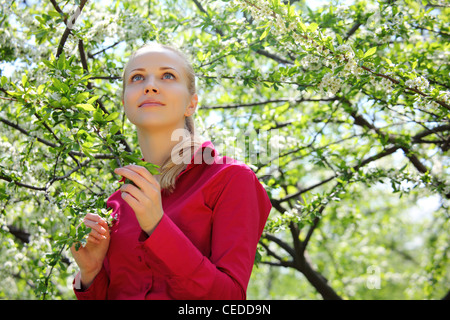 schöne Blondine sieht nach oben im blühenden Garten im Frühjahr Stockfoto