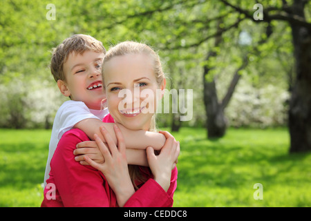 Sohn umarmt hinter Mutter für Hals im Park im Frühjahr Stockfoto