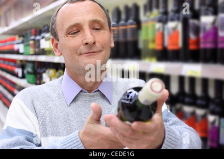 glücklicher älterer Mann im Shop blickt auf Flasche Wein in Händen Stockfoto