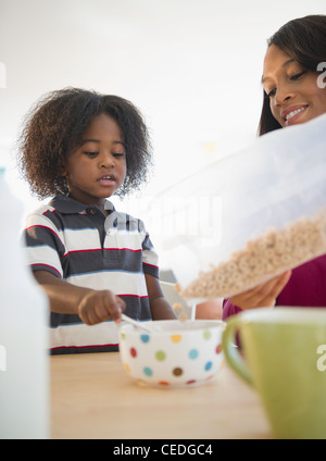 African American Mutter Gießen Getreide für Sohn Stockfoto