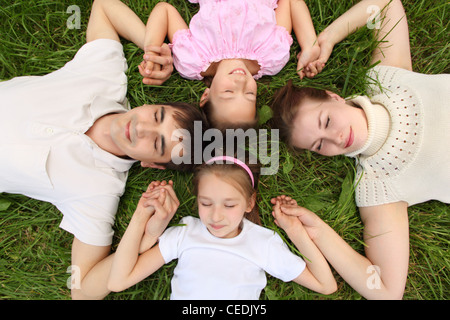 Eltern mit Kindern liegen auf dem Rasen, Ansicht von oben, Kopf an Kopf, Händen beigetreten Stockfoto
