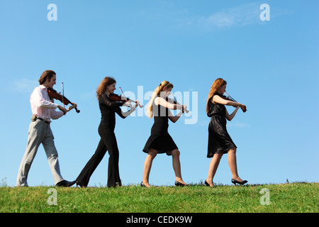 Vier Musiker gehen und spielen Geigen gegen Himmel, Seitenansicht Stockfoto