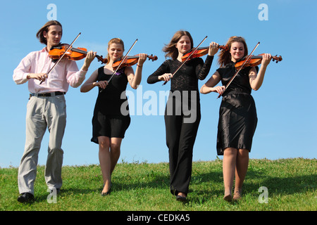 Vier Musiker gehen und spielen Geigen gegen Himmel, Frontansicht Stockfoto