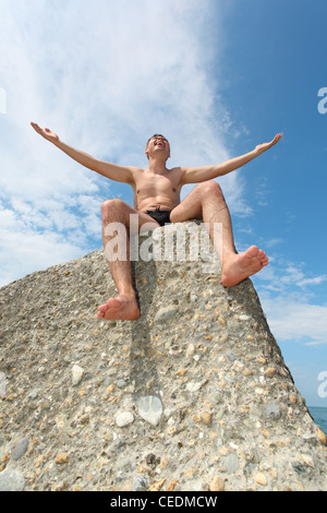 Mann in rutscht sitzt auf Fels, Ansicht von unten Stockfoto