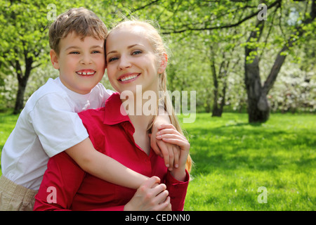 Sohn umarmt hinter Mutter im Park im Frühjahr Stockfoto